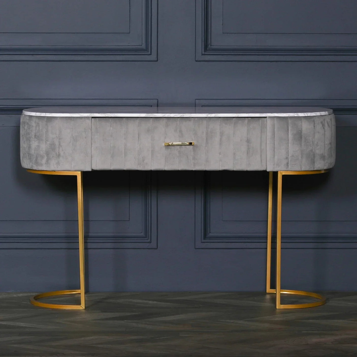 Grey velvet console table with gold legs and marble effect top against dark blue wall