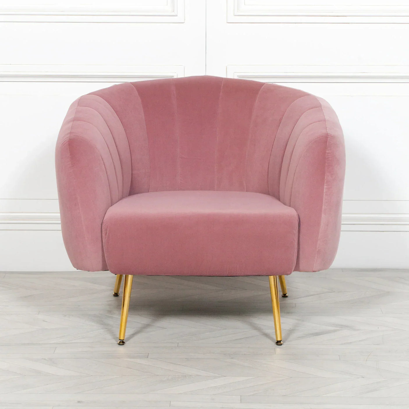 Pink velvet armchair with gold metal legs on light wood floor, front view