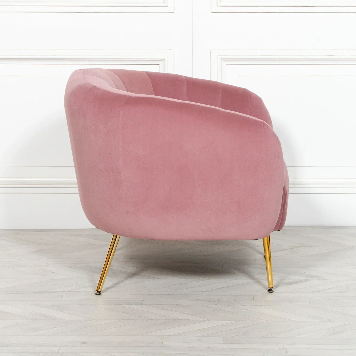 Side view of pink velvet accent chair with gold legs on wooden floor