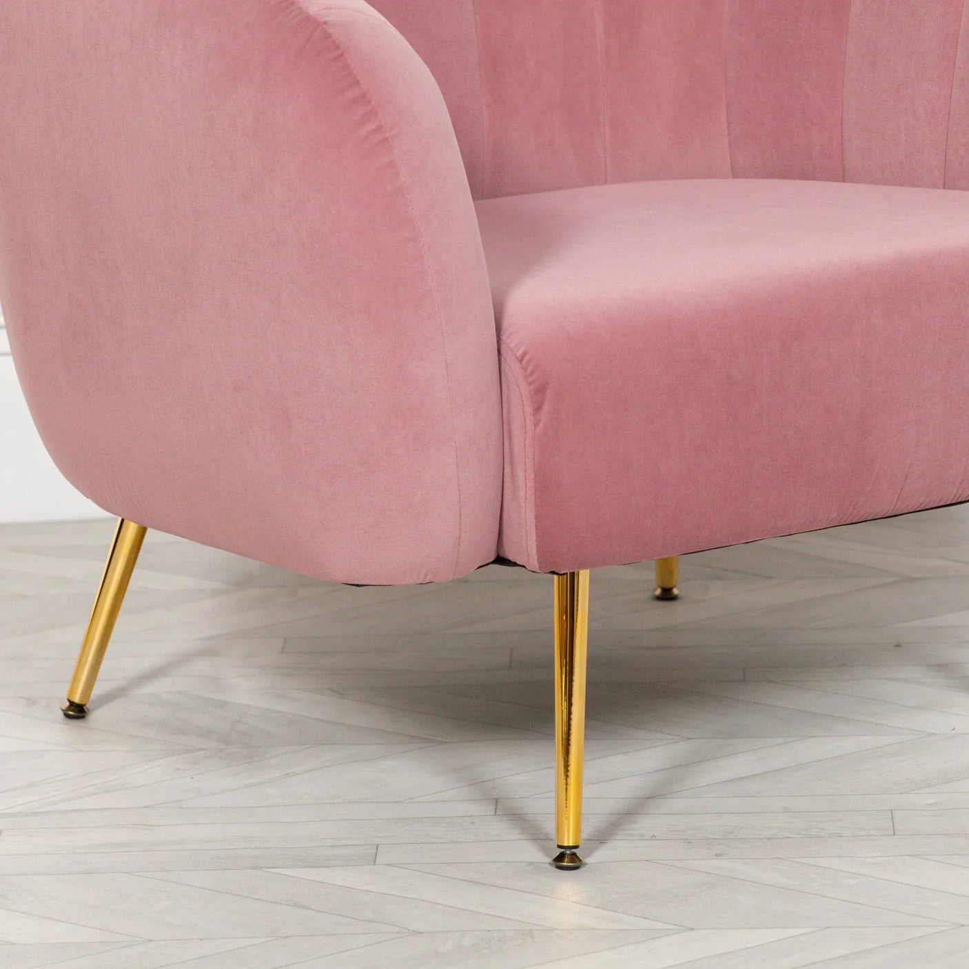 Pink velvet sofa with gold metal legs on light wood floor, angled side view