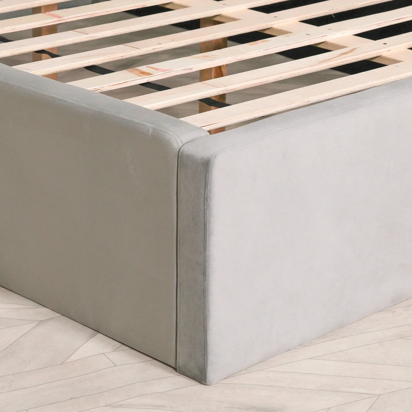 Close up of grey upholstered bed frame corner with wooden slats visible