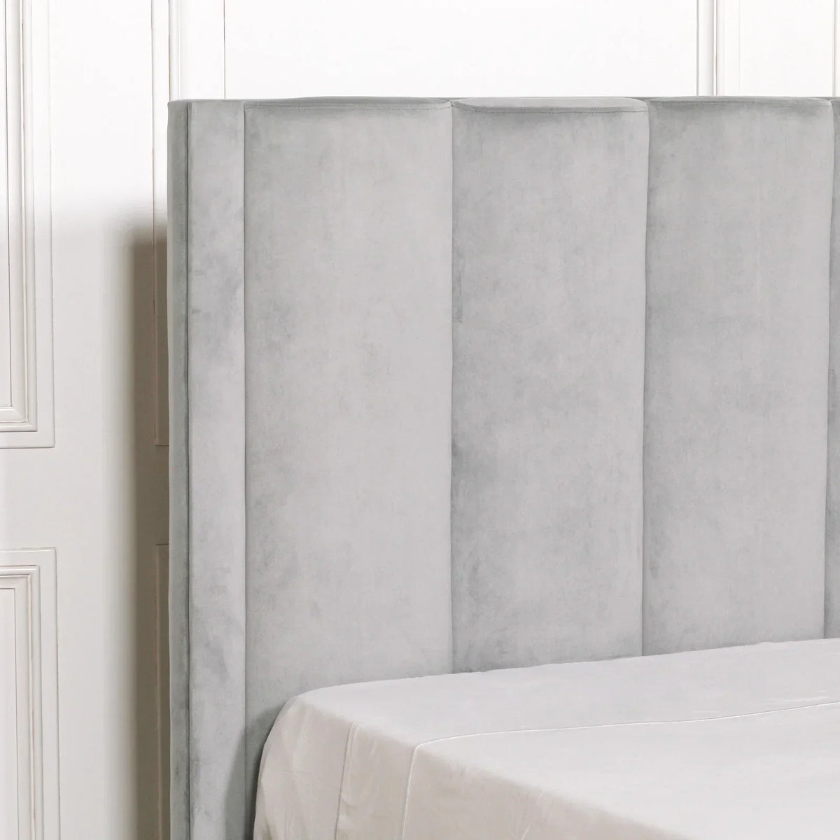 Light grey velvet upholstered headboard with vertical panel detail beside white bedding