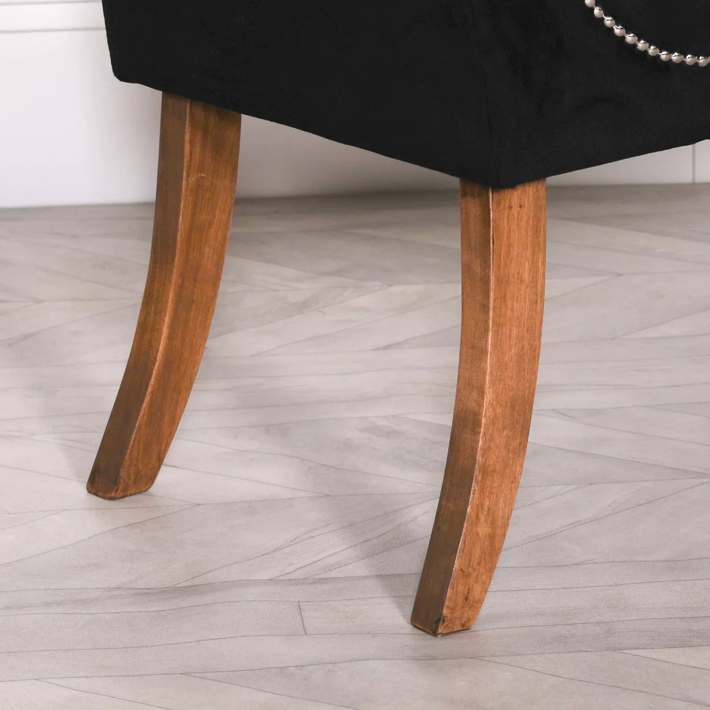Close-up of two wooden curved chair legs with black upholstered seat and stud detail