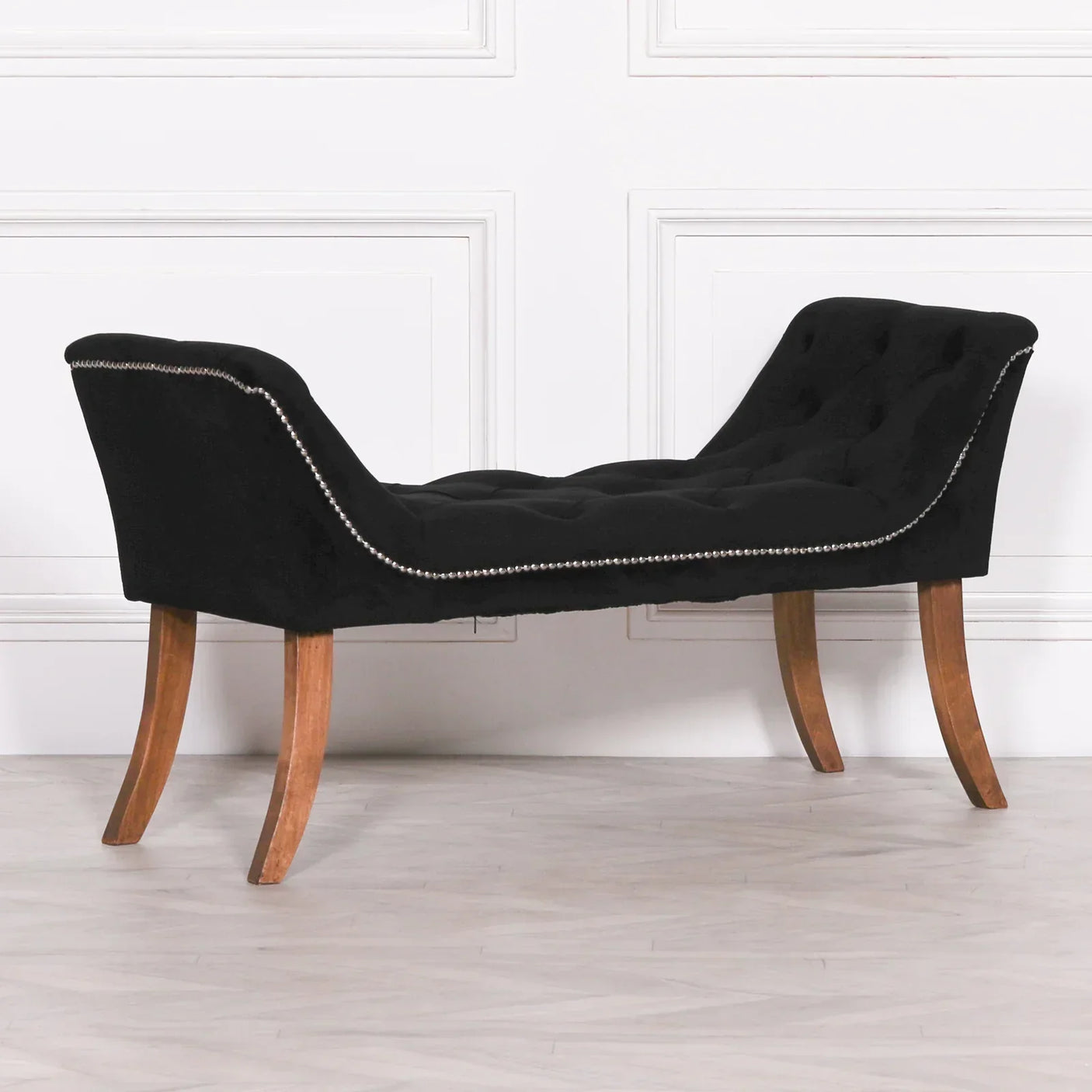 Black upholstered bench with wooden legs and silver stud detailing against white panel wall