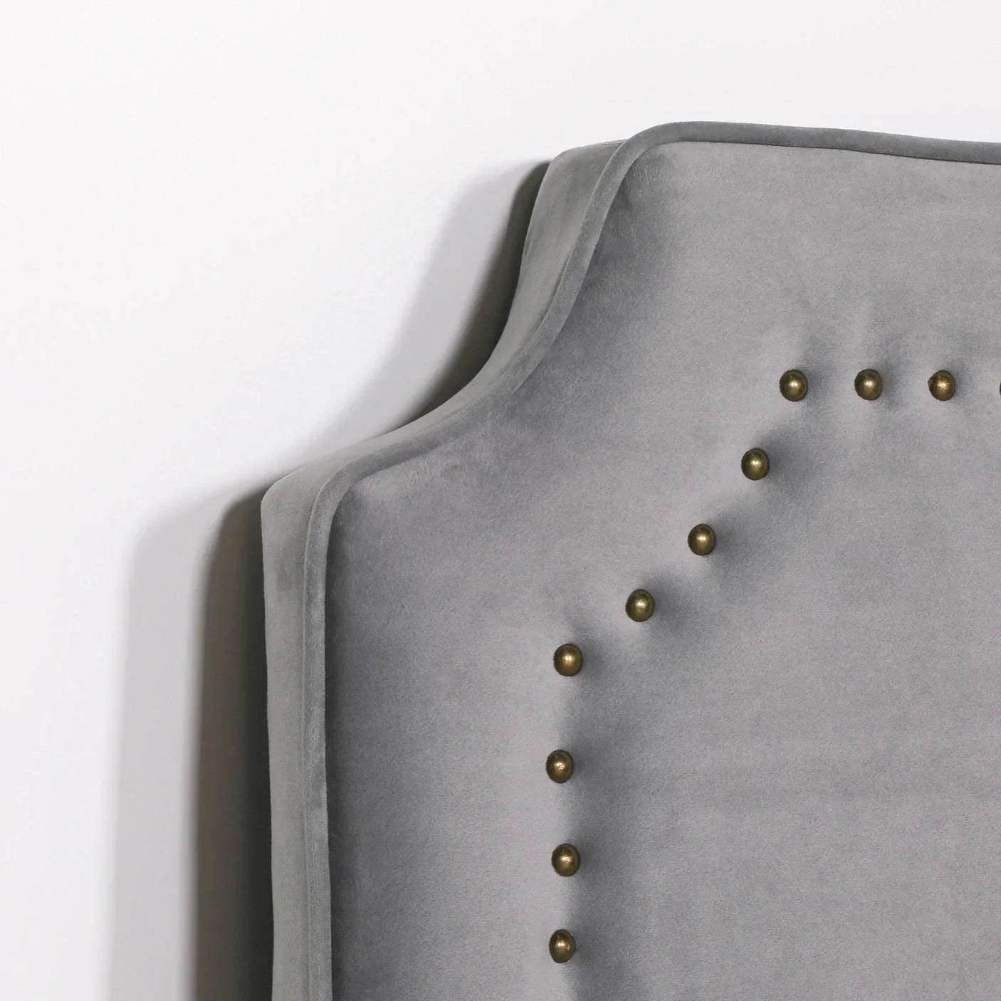 Grey velvet headboard with brass stud detailing, close-up of corner and texture