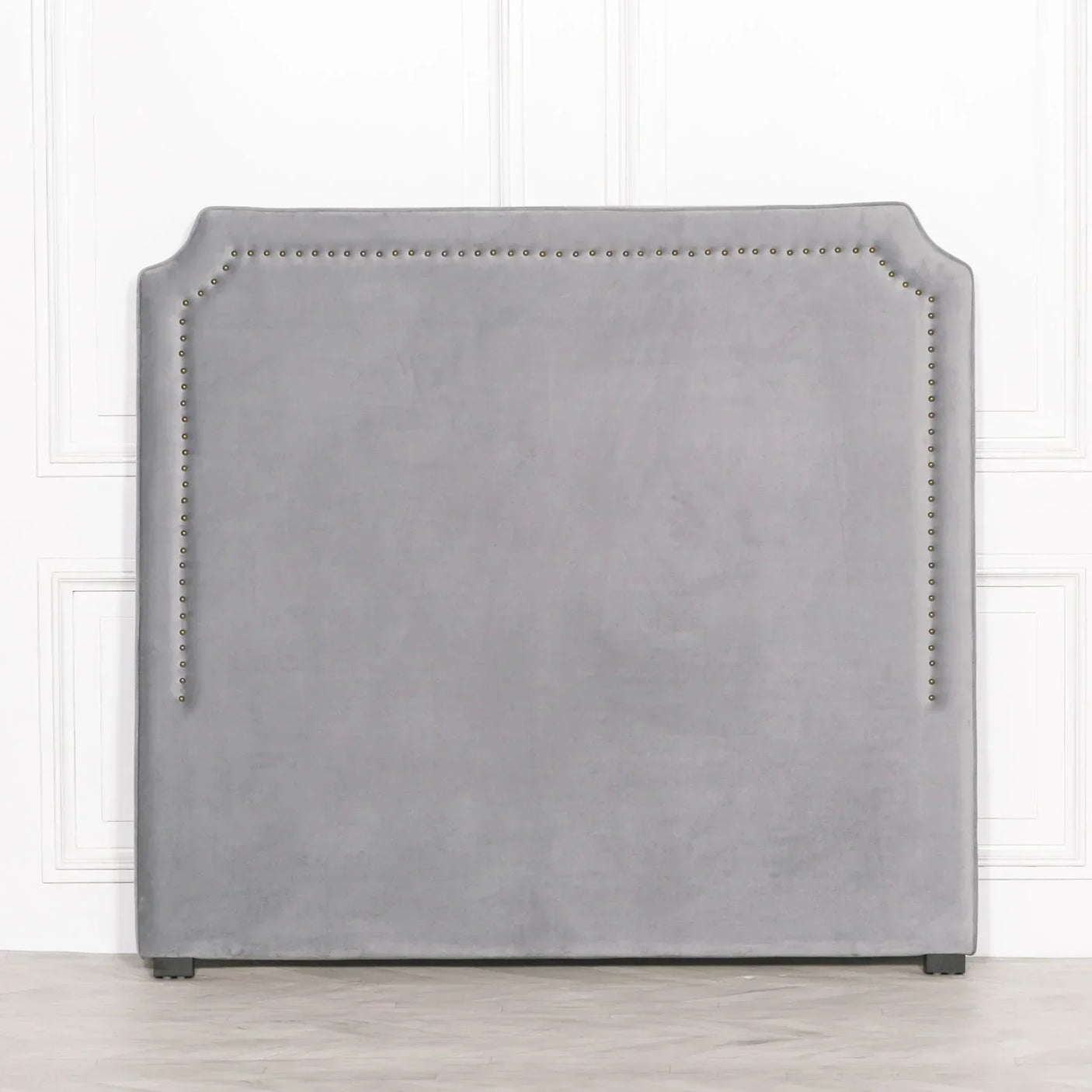 Grey velvet headboard with nailhead trim detail against a white panelled wall