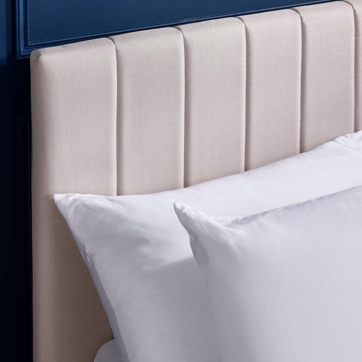 Beige upholstered headboard with vertical panels and white bedding against blue wall