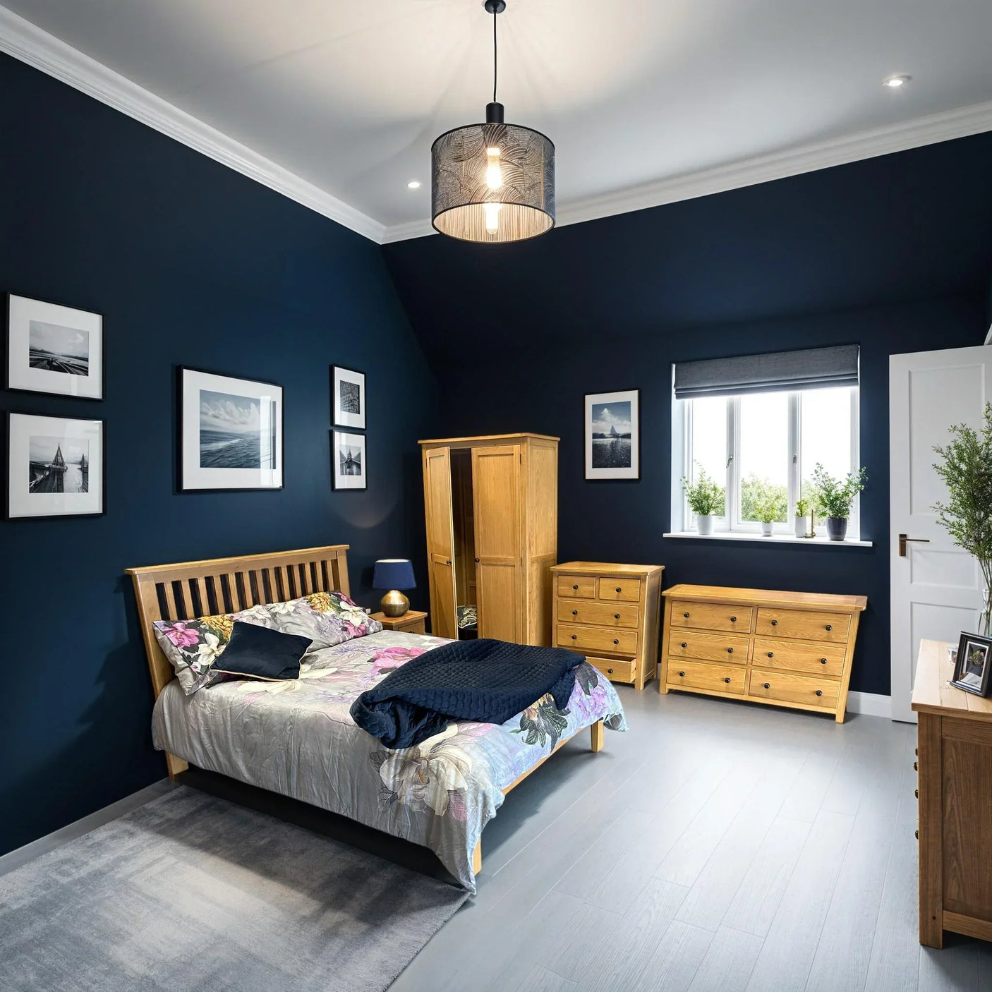 Oak bedroom furniture set with wardrobe, bed, and dressers against navy blue walls