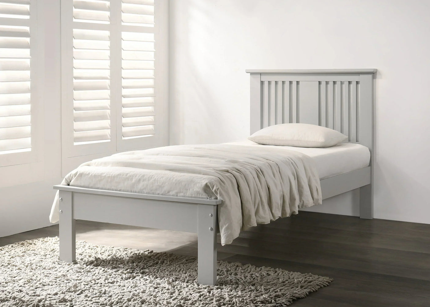 Grey wooden single bed with slatted headboard, white bedding and textured rug in bright room