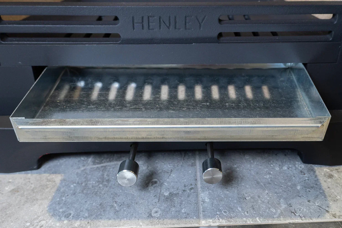 Metal ash tray and control knobs on black solid fuel stove