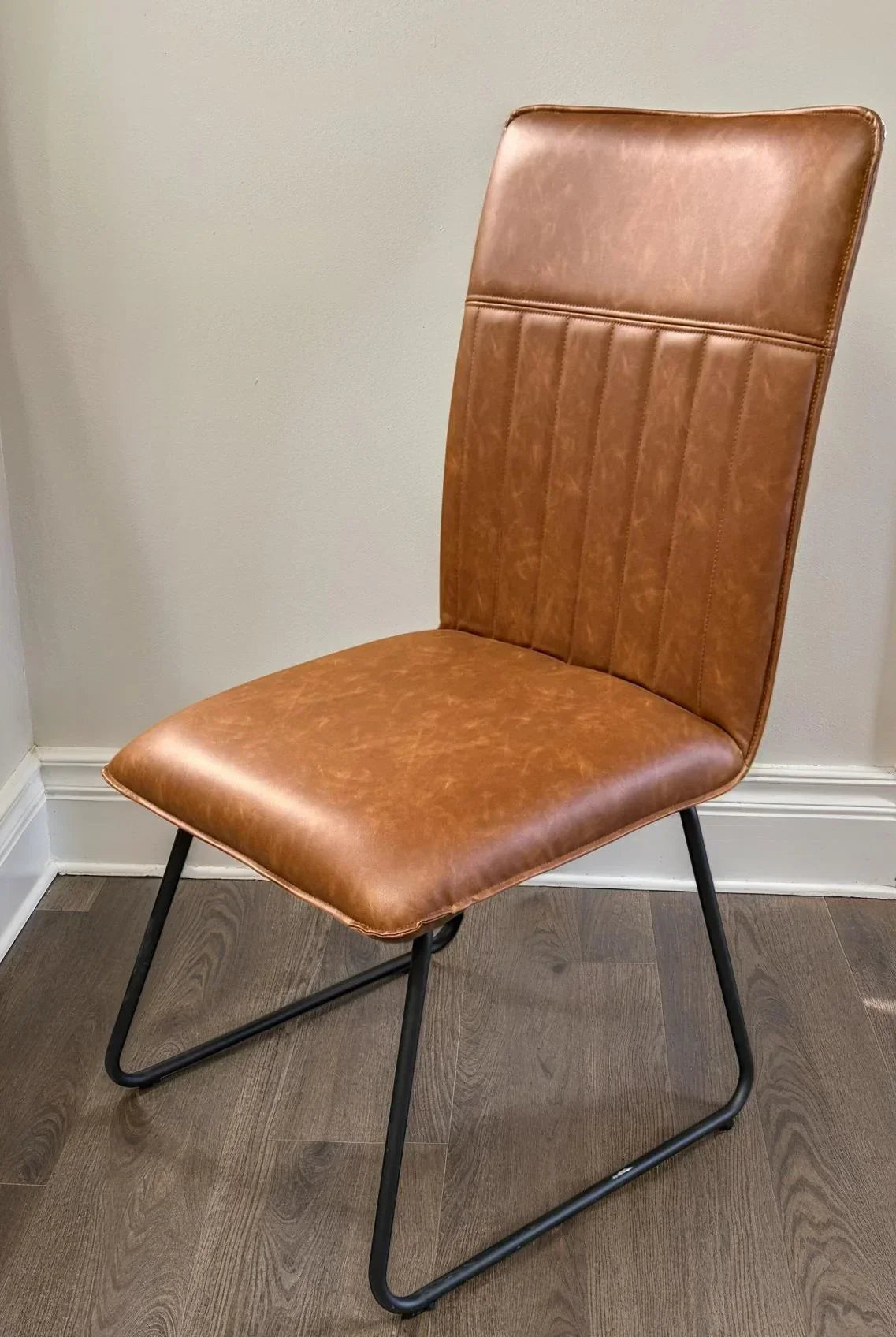 Cognac leather dining chair with metal legs and stitched backrest on wood floor