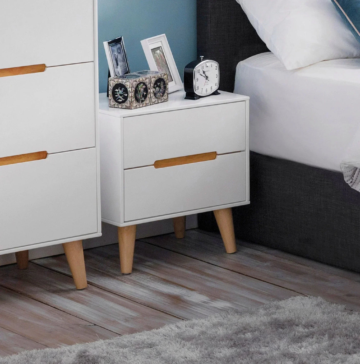 White two drawer bedside table with wooden legs next to bed on wooden floor