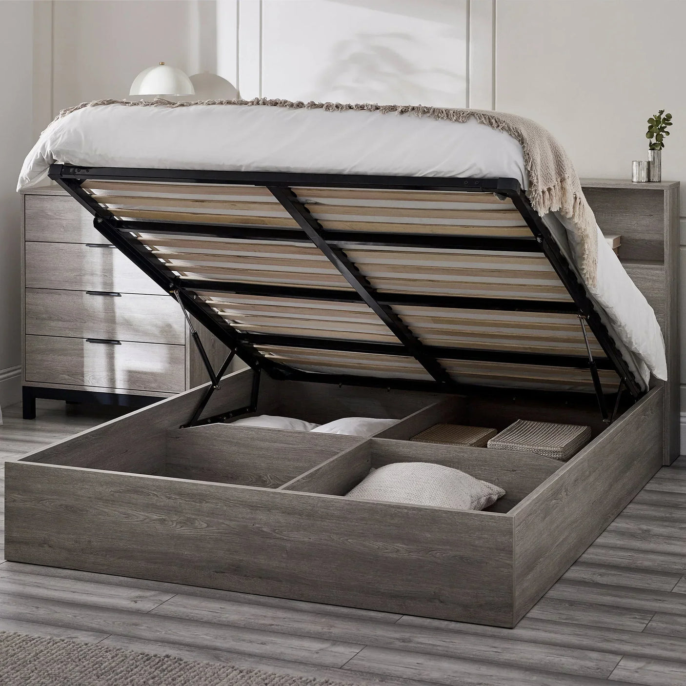Grey oak ottoman bed with gas lift open, showing underbed storage compartments in bedroom