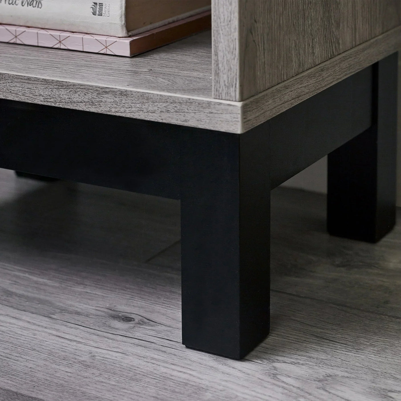 Grey oak bedside table corner with black legs and shelf holding books