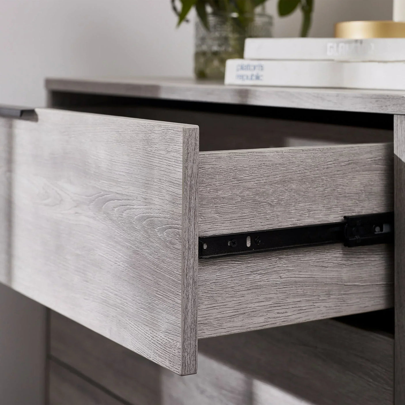 Closeup of grey oak chest of drawers with open drawer and metal runners