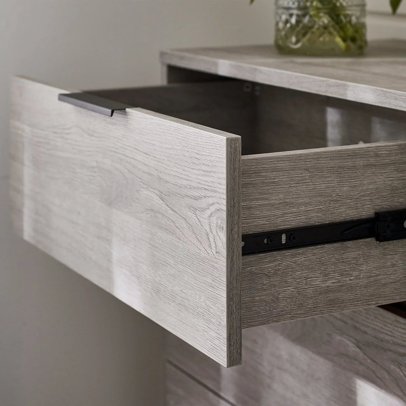 Light oak chest of drawers close-up showing open drawer and metal handle detail