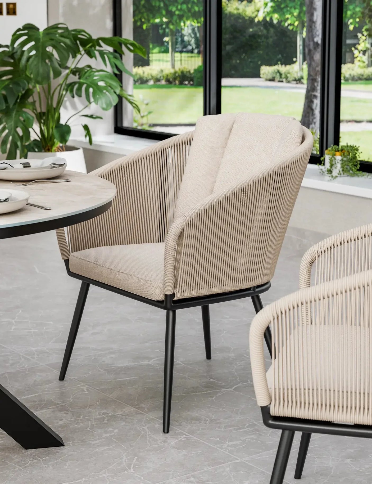Beige rope dining chair with black legs beside modern round table in bright dining room