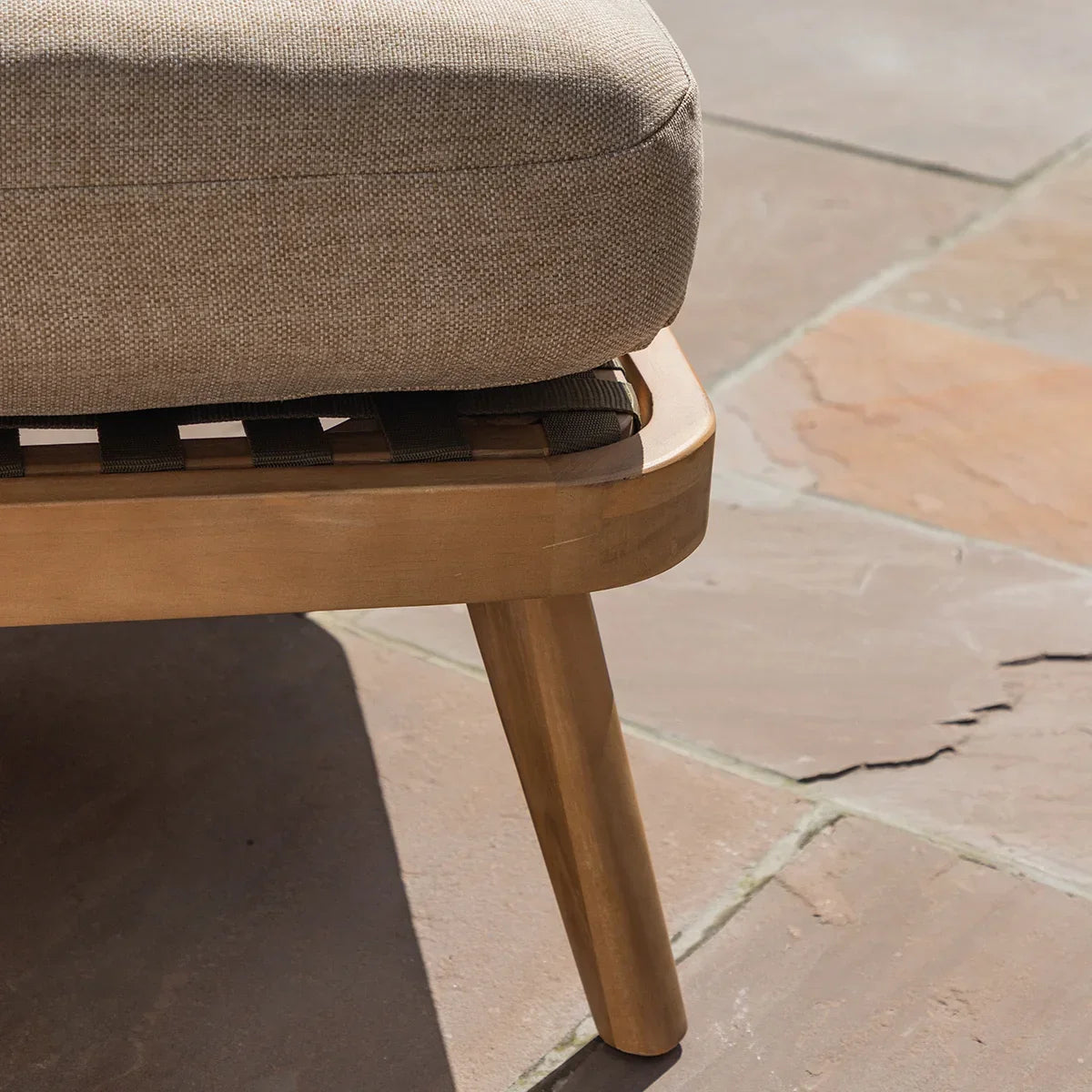 Close-up of wooden garden sofa leg with beige cushion on stone patio