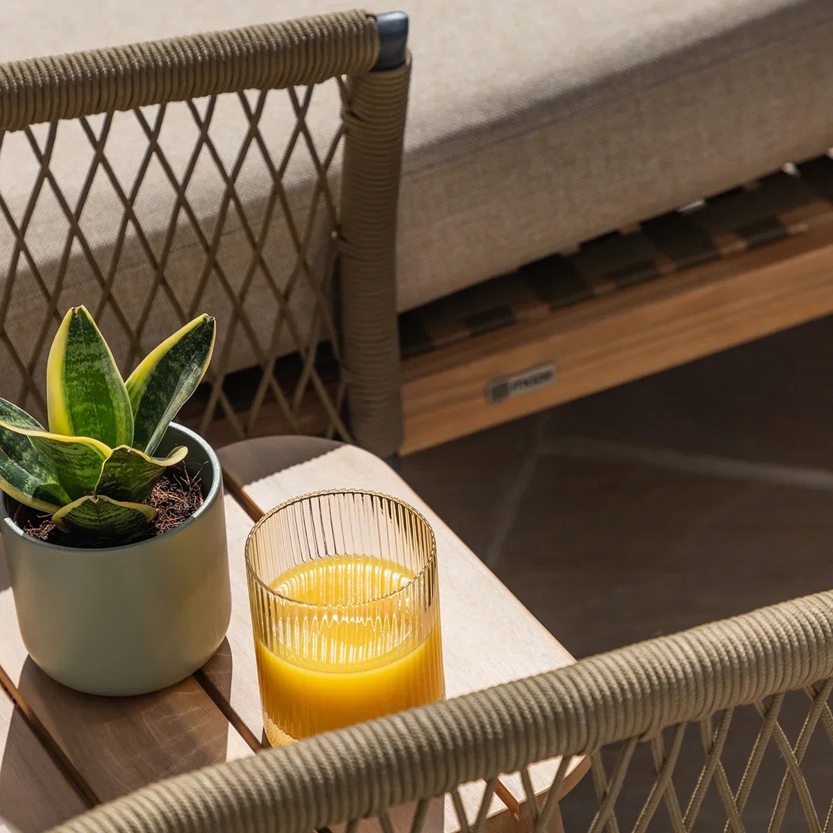 Outdoor rope sofa set with beige cushion, side table, plant and glass of orange juice
