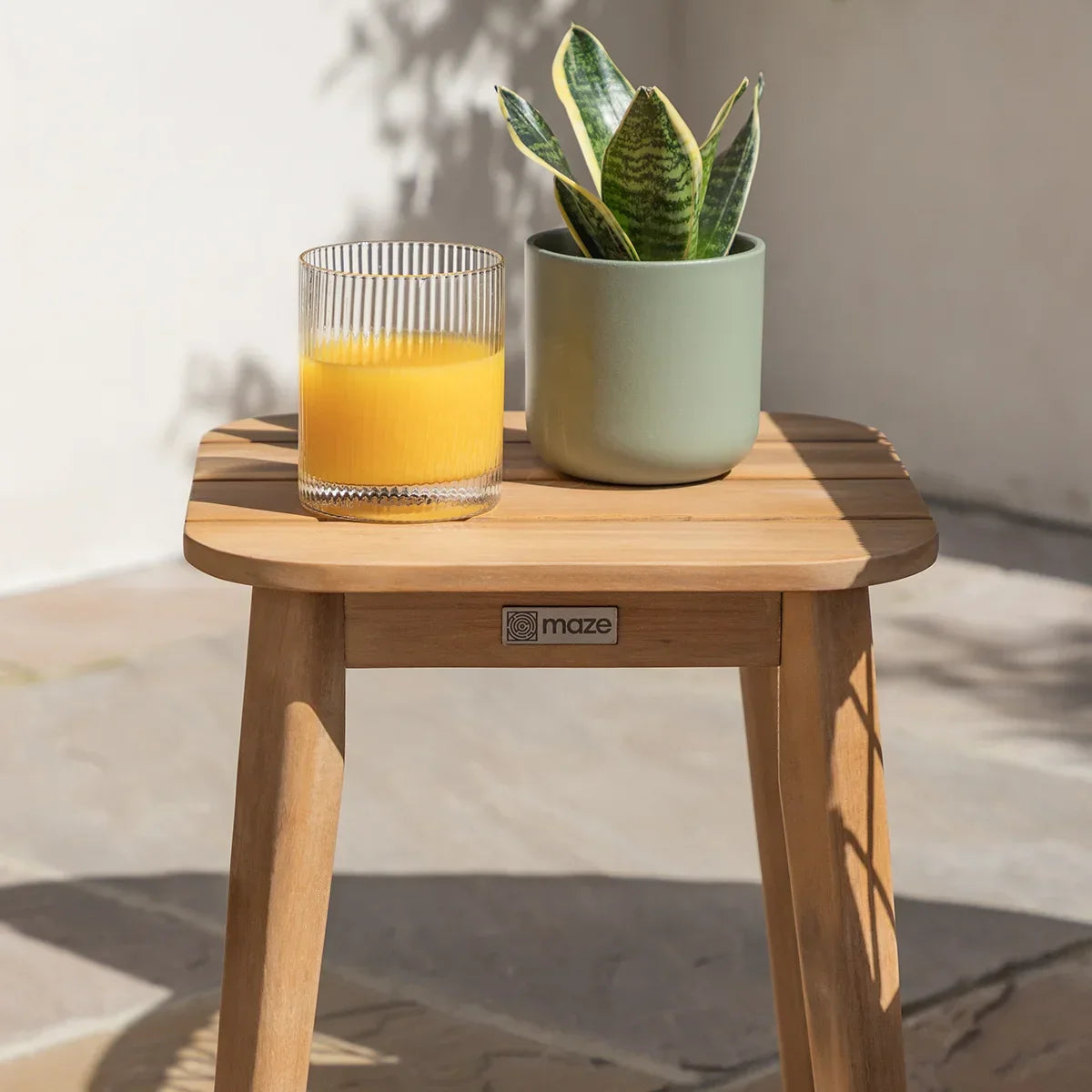 Teak side table with potted plant and glass of orange juice on outdoor patio
