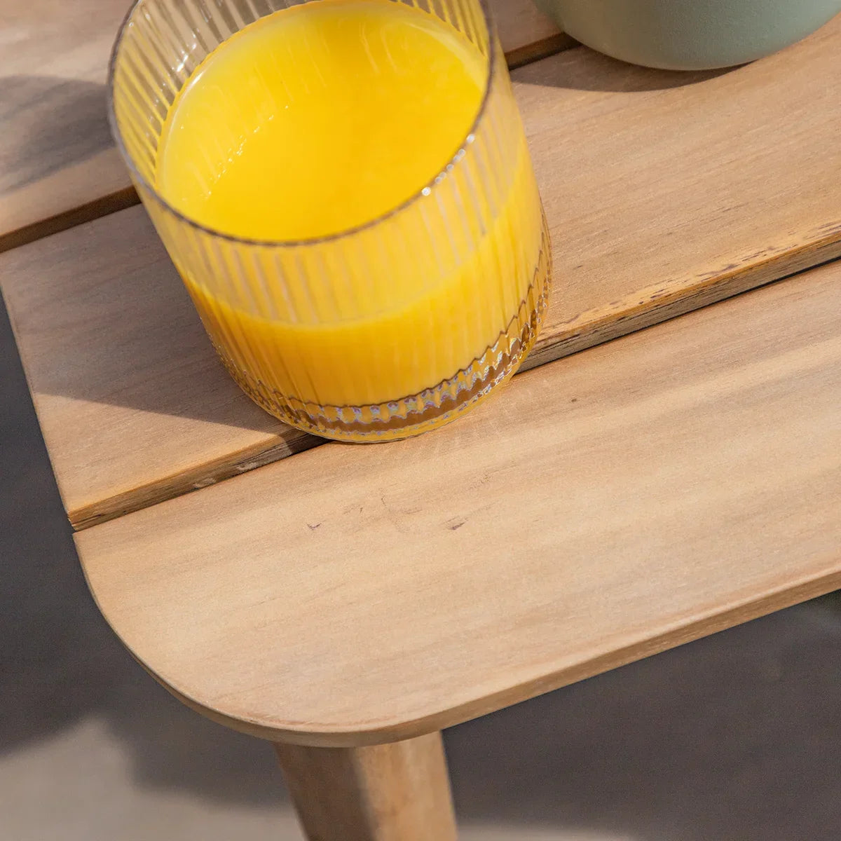 Closeup of light wooden outdoor side table with glass of orange juice on top