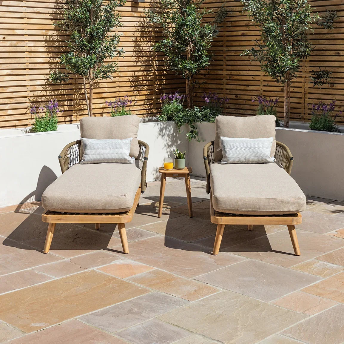 Pair of beige outdoor sun loungers with cushions and side table on patio