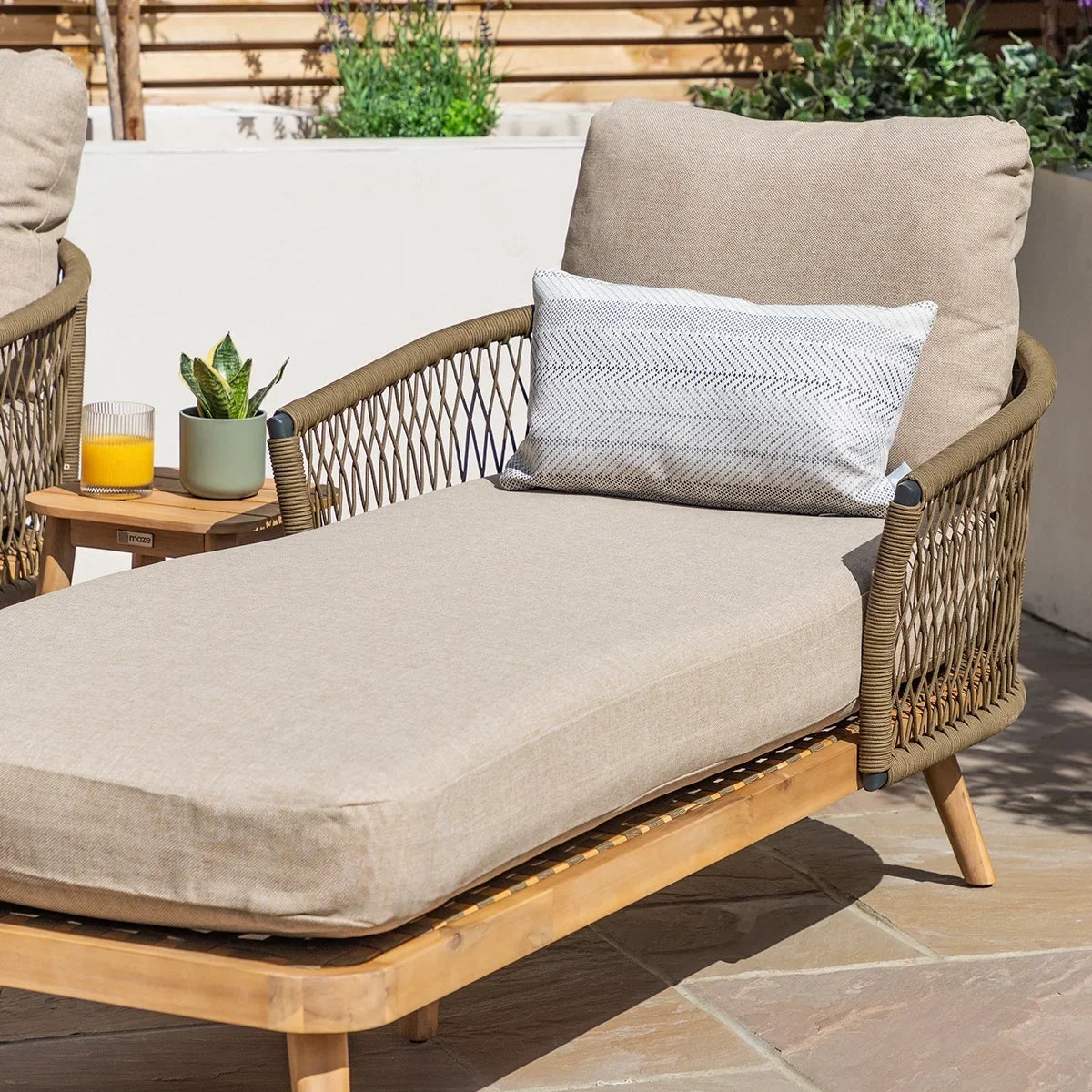 Beige outdoor rattan sun lounger with cushion, armrest detail, and side table on patio
