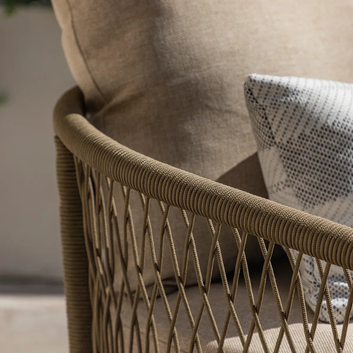 Close-up of outdoor woven rope sofa arm with beige cushion and patterned throw pillow