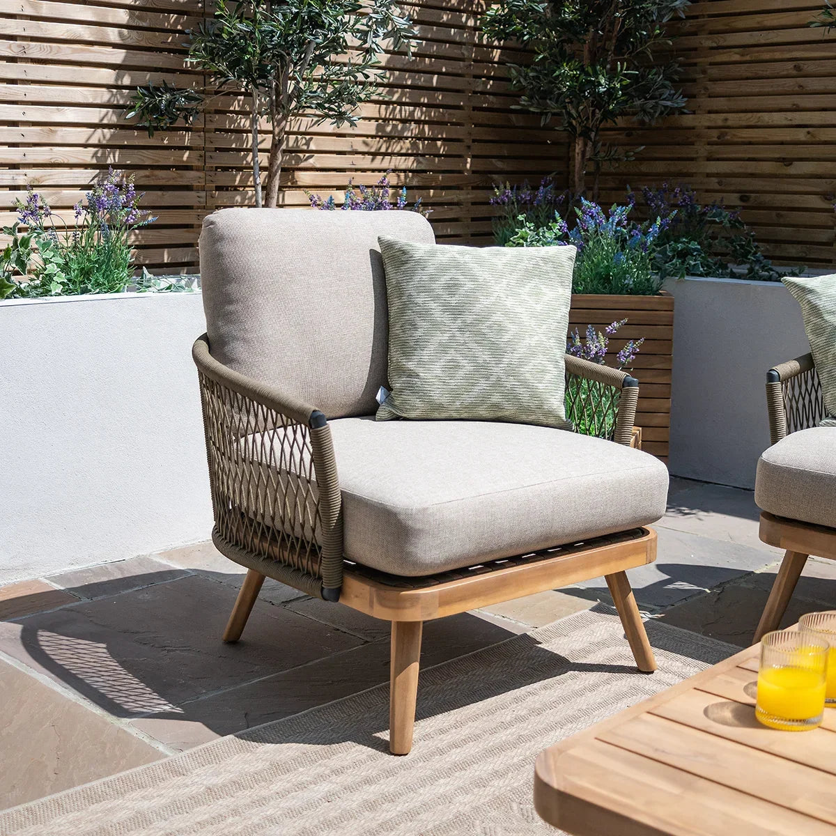 Beige outdoor garden armchair with rope sides and green cushion on patio setting