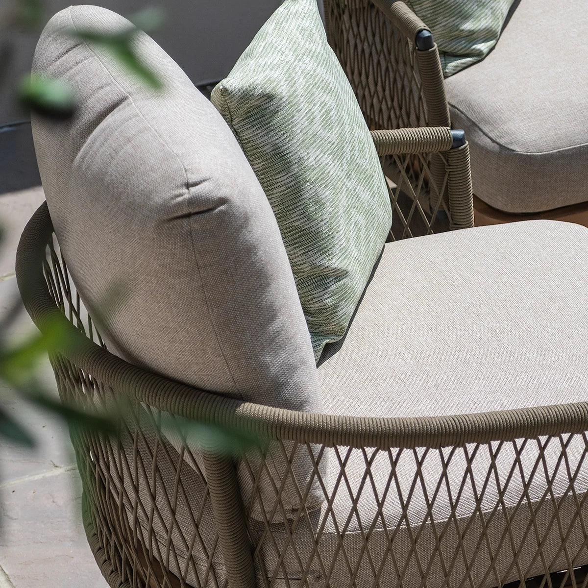 Outdoor lounge chair with beige cushions and green accent pillow, rope mesh frame detail