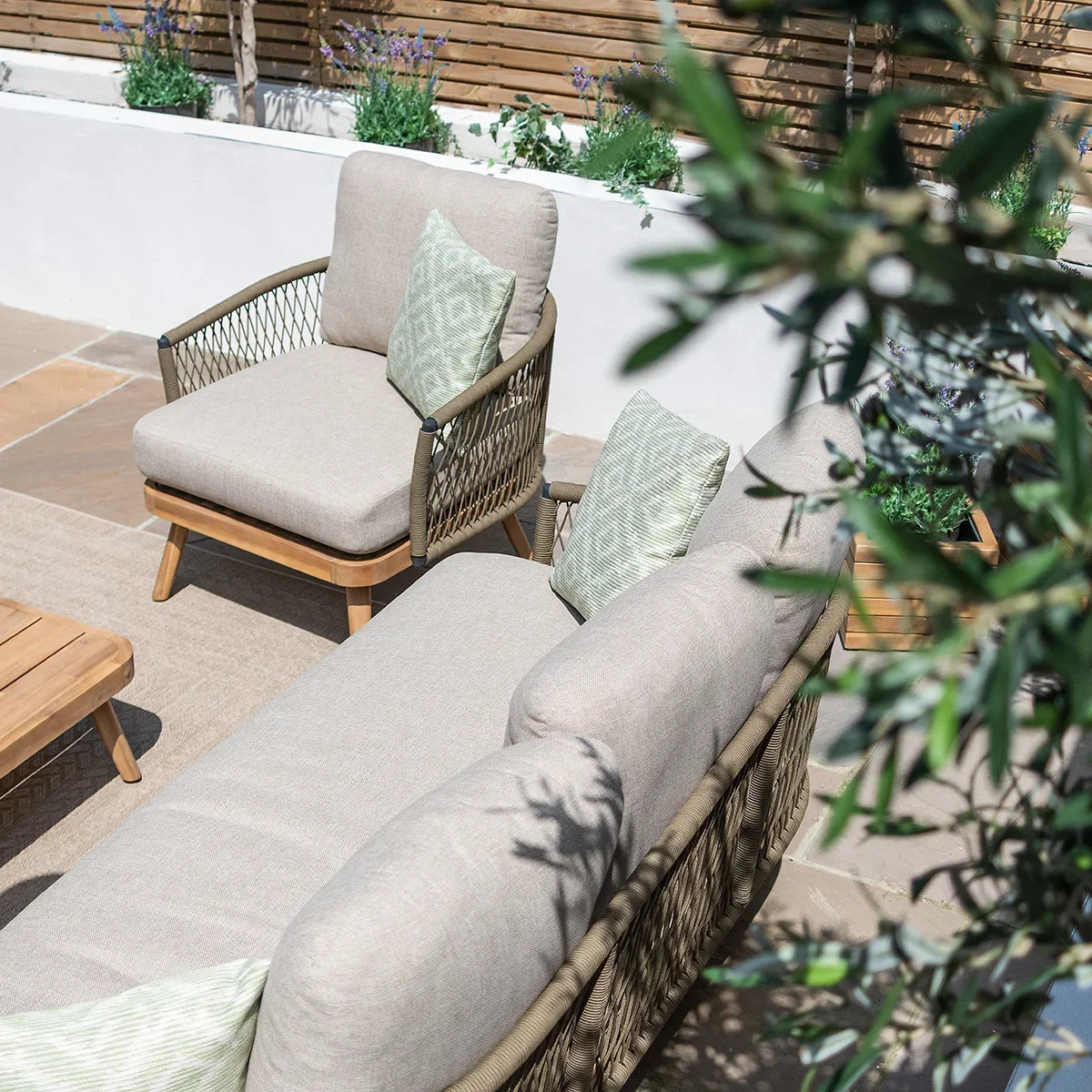 Beige outdoor sofa set with rope detailing, matching armchair and green cushions on patio