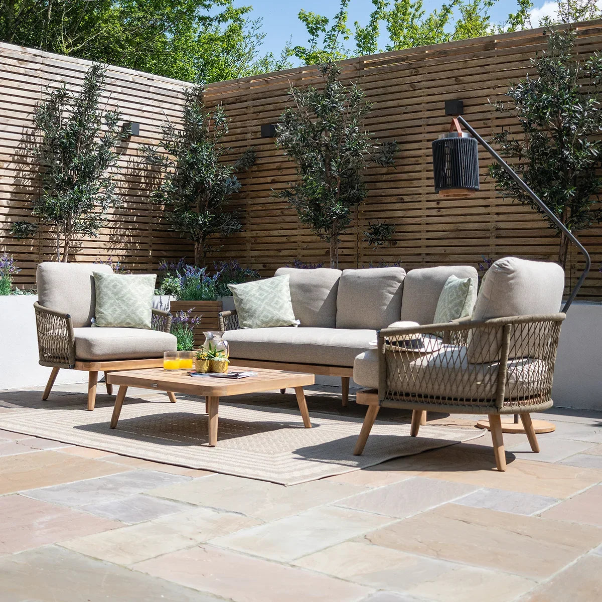 Outdoor rattan sofa set with beige cushions, armchair and table on patio with wooden screen