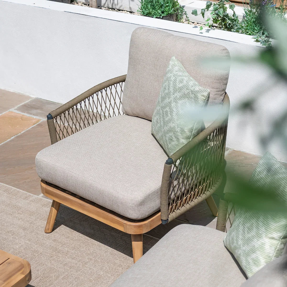 Beige outdoor armchair with rope sides, wooden legs and green cushion on patio