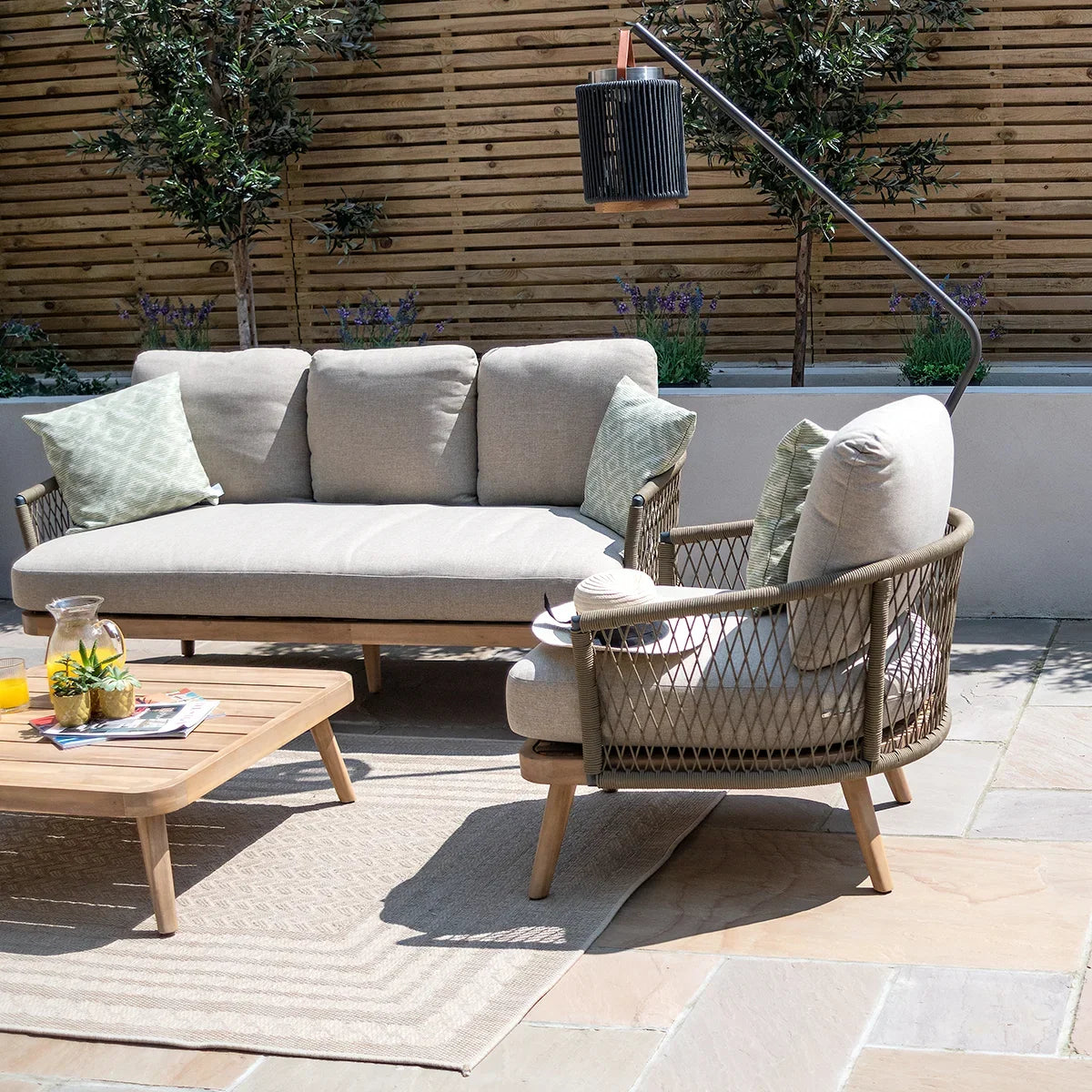 Beige rattan outdoor sofa set with armchair and coffee table on a stone patio