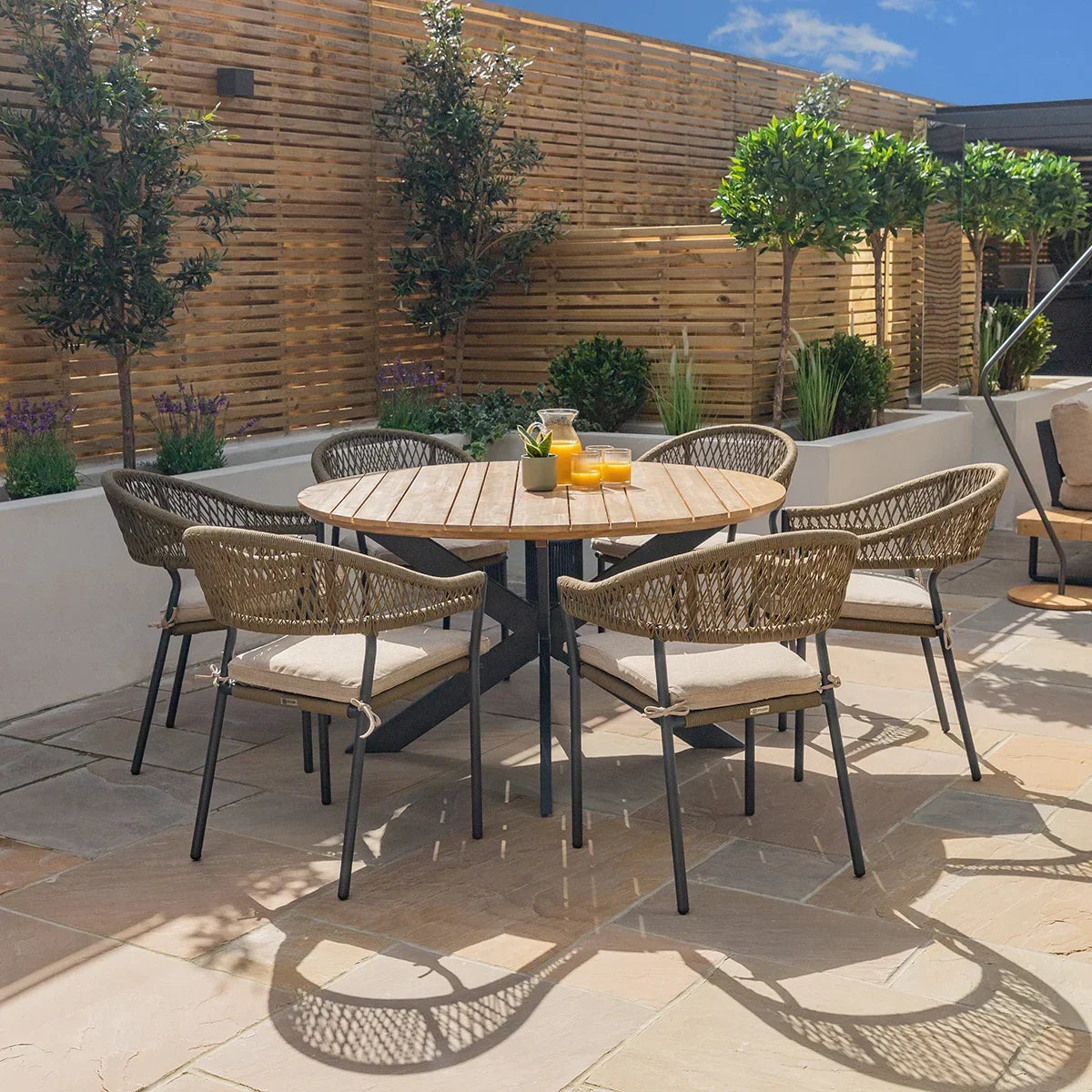 Round wooden garden dining table with woven armchairs on a patio setup