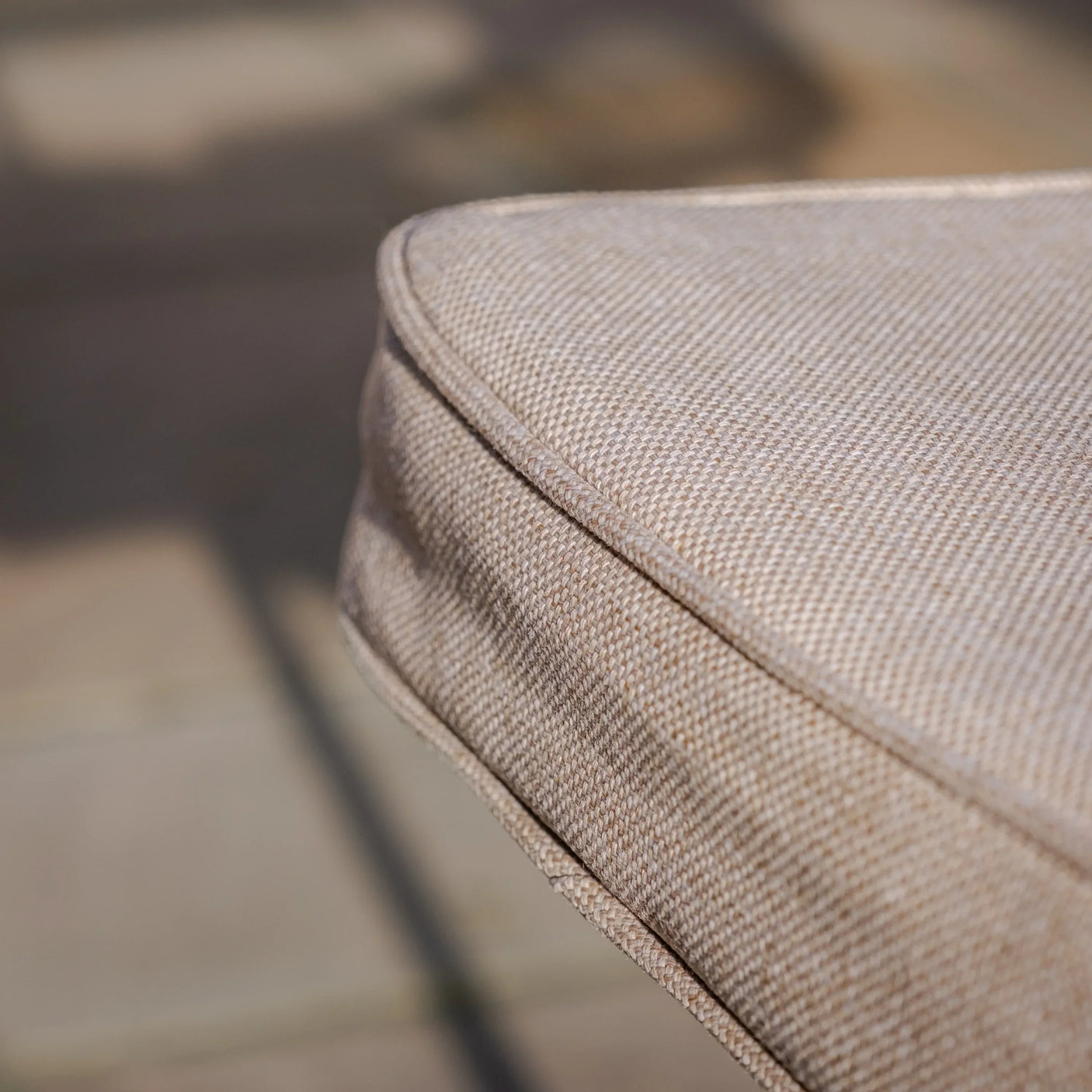 Close-up of beige outdoor sofa cushion with textured fabric and piped edge