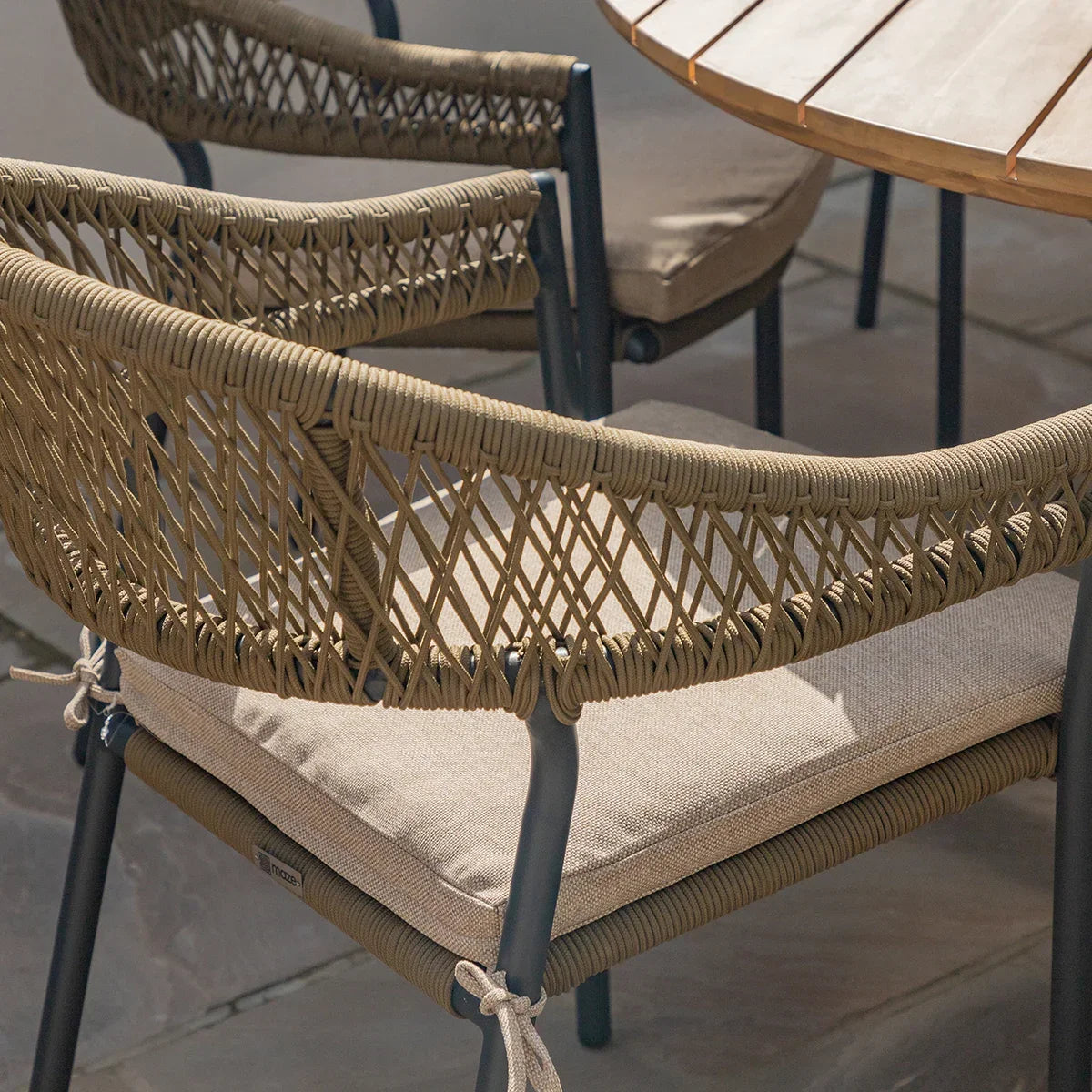 Outdoor dining chair with woven rope back and taupe cushion beside wooden patio table