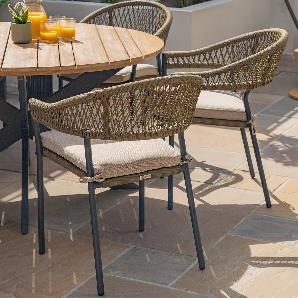 Round wooden patio dining table with rope weave garden chairs and beige seat cushions