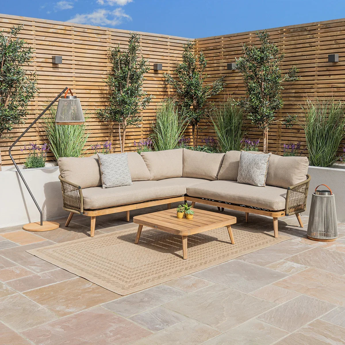 Beige outdoor corner sofa set with wooden coffee table on a patio, surrounded by greenery