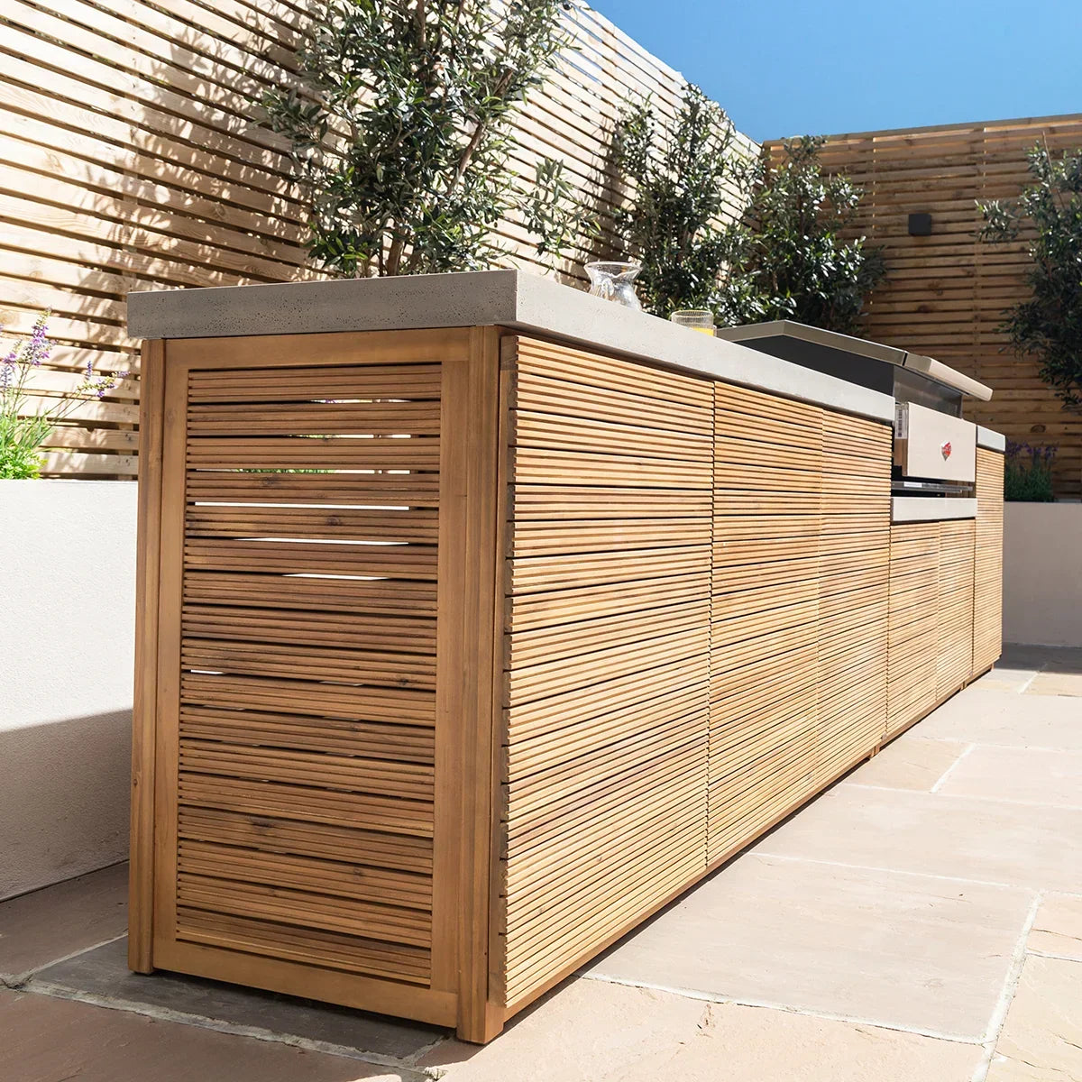 Outdoor kitchen unit with teak slatted panels and stone countertop in garden setting