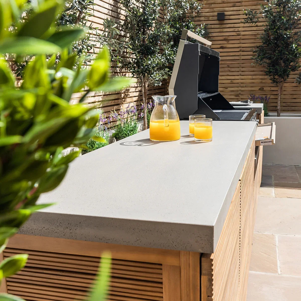 Outdoor kitchen unit with concrete countertop and grill, glass jug and drink on surface