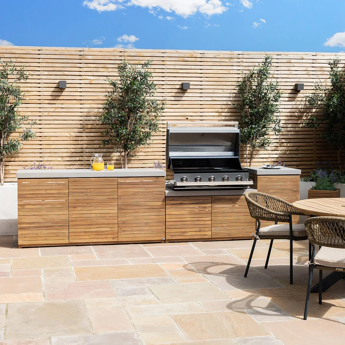 Outdoor kitchen with wooden cabinets, built-in gas barbecue grill, patio chairs and dining table