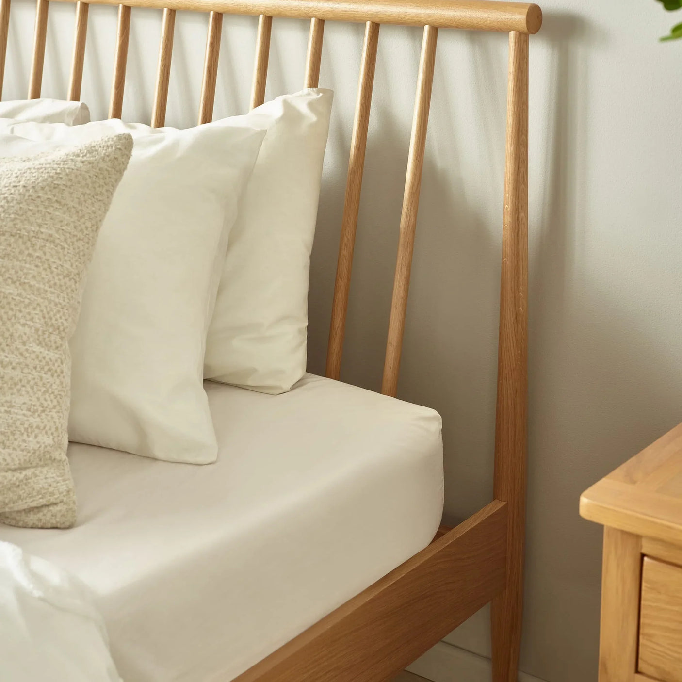 Oak wooden bed frame with spindle headboard and cream bedding next to matching bedside table
