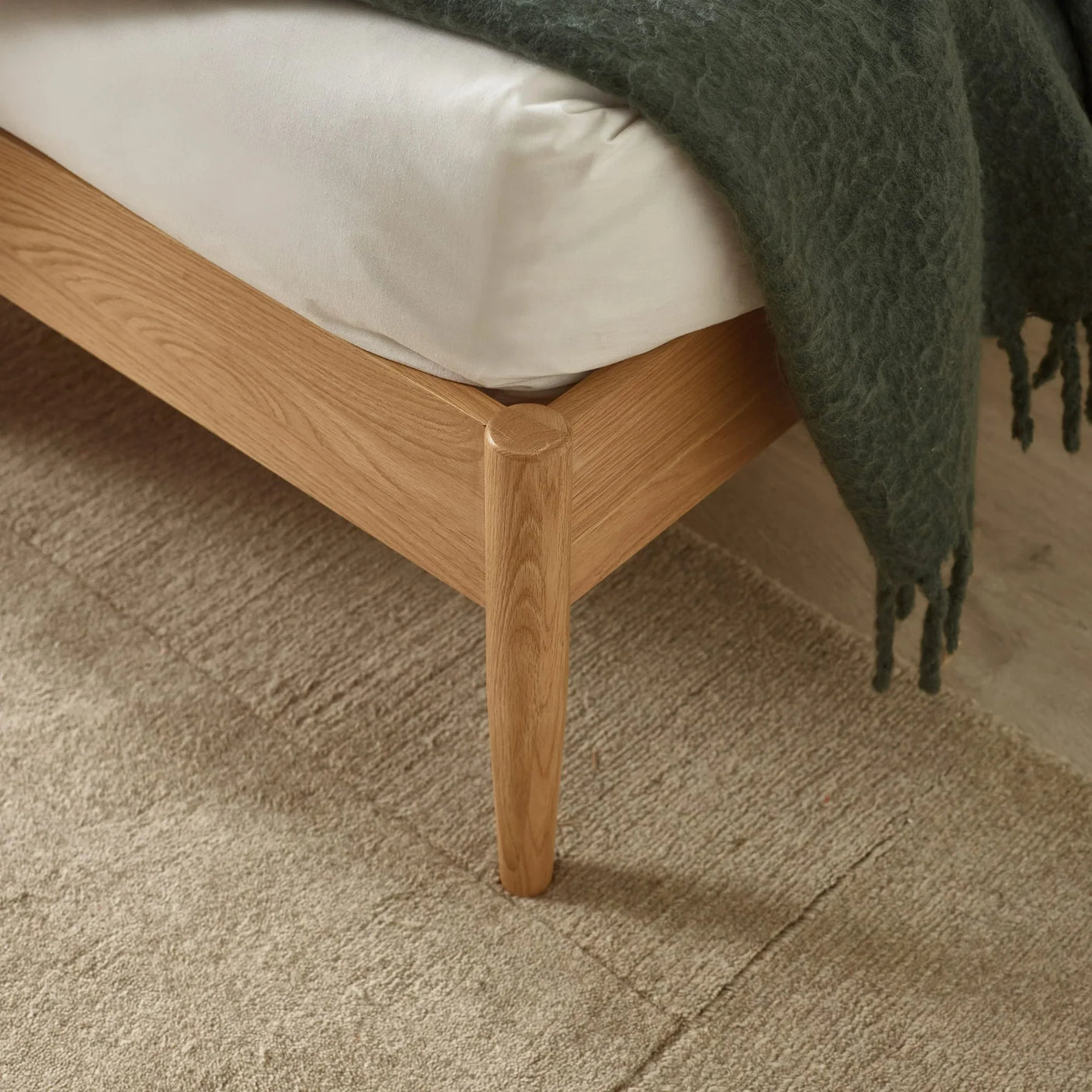 Close view of oak bed frame corner with white mattress and textured green throw blanket