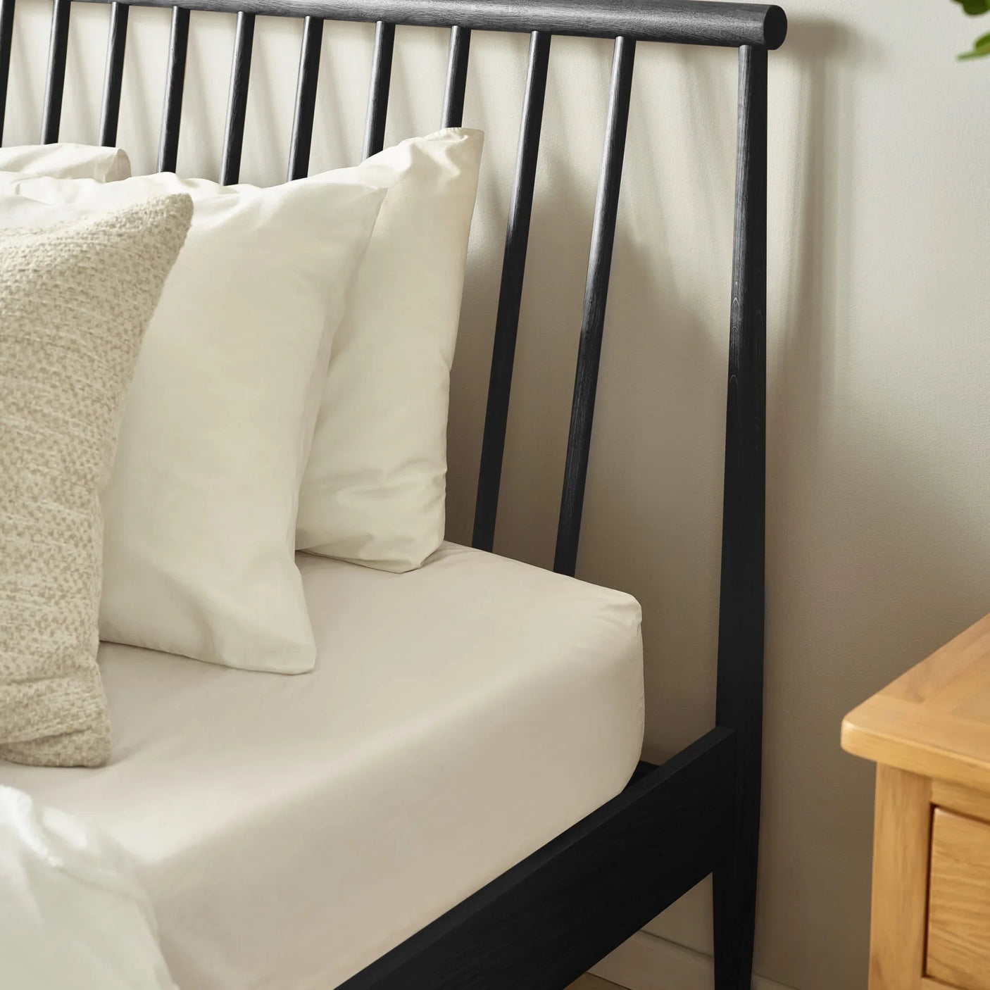 Black metal bed frame with vertical slats, cream bedding, and wooden bedside table
