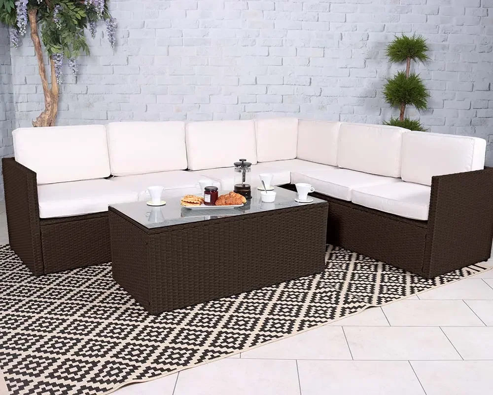 Brown rattan corner sofa set with cream cushions and glass coffee table on patterned rug