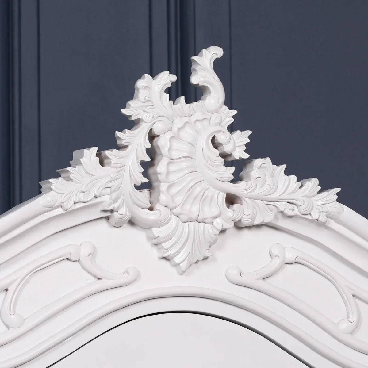 White carved wooden headboard with ornate floral detailing against dark wall panel