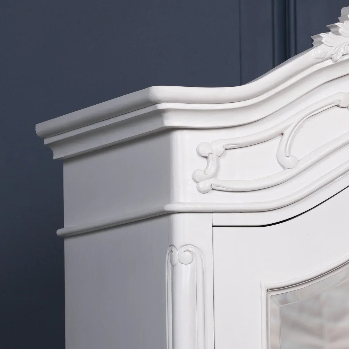 White wooden wardrobe corner with ornate carved details against a blue wall