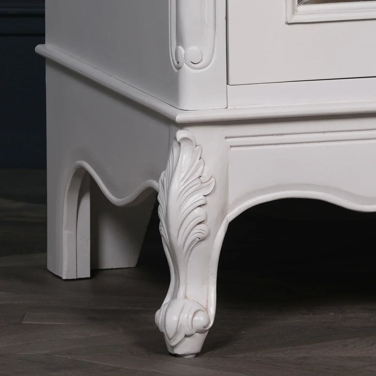 White wooden bedside table with carved ornate leg detail on dark wood floor