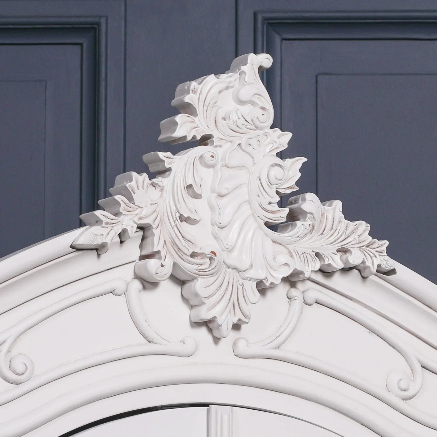 White ornate wood wardrobe cornice with carved detailing against blue panelled wall